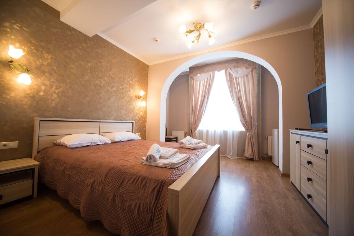 A bedroom with a large bed, a nightstand, a dresser, and a television.