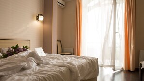 A neatly made bed with white linens and a laptop on it, a chair, and a window with sheer curtains. - Hotel Kolyda (Sovinion)