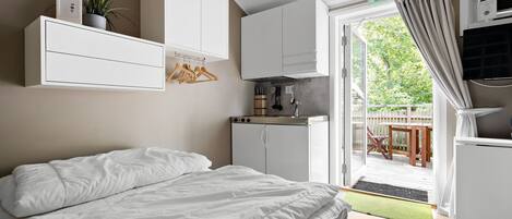 A bedroom with a bed, a wardrobe, a kitchenette, and a sliding glass door to an outdoor area.