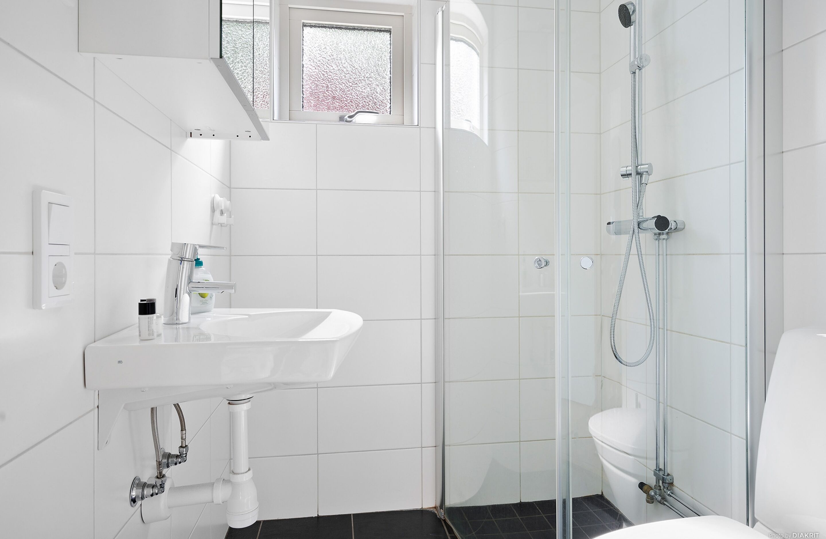 A modern bathroom with a white sink, a glass shower enclosure, and a small window above the sink.