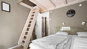 Un dormitorio con una escalera de madera que conduce a una puerta, una cama con ropa blanca, un reloj en la pared y un aviso en un marco en la pared.