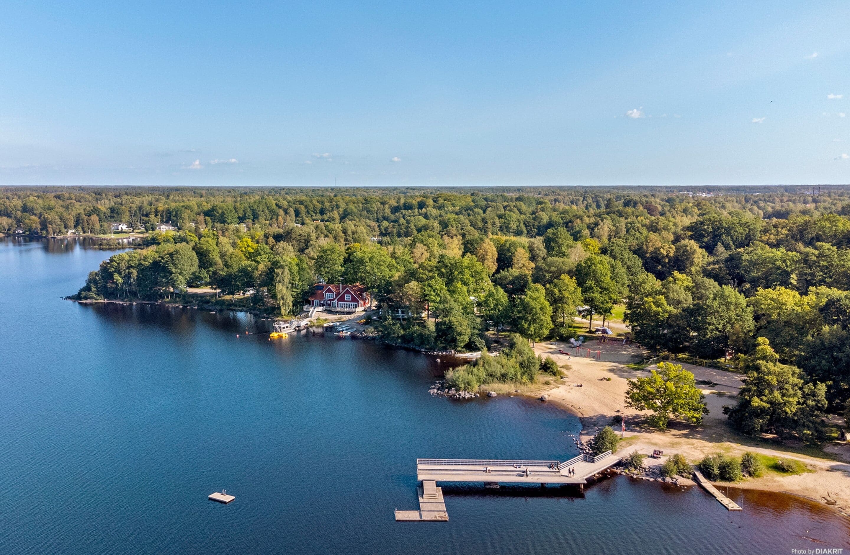 An aerial view of a lakeside property with a dock, a house, and surrounding forest.