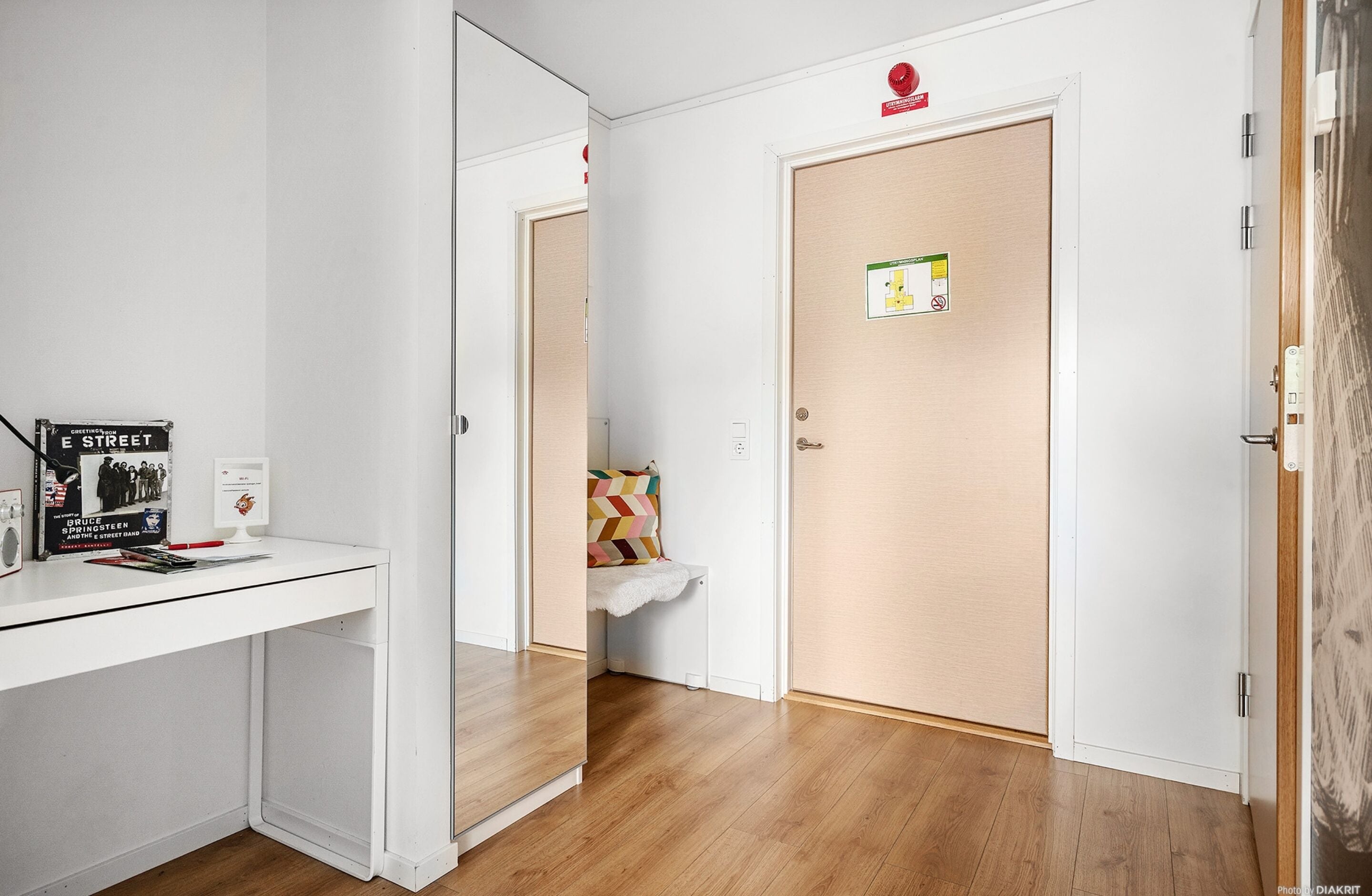 A hallway with a white desk, a door with a safety sign, and a bench with a colorful cushion.