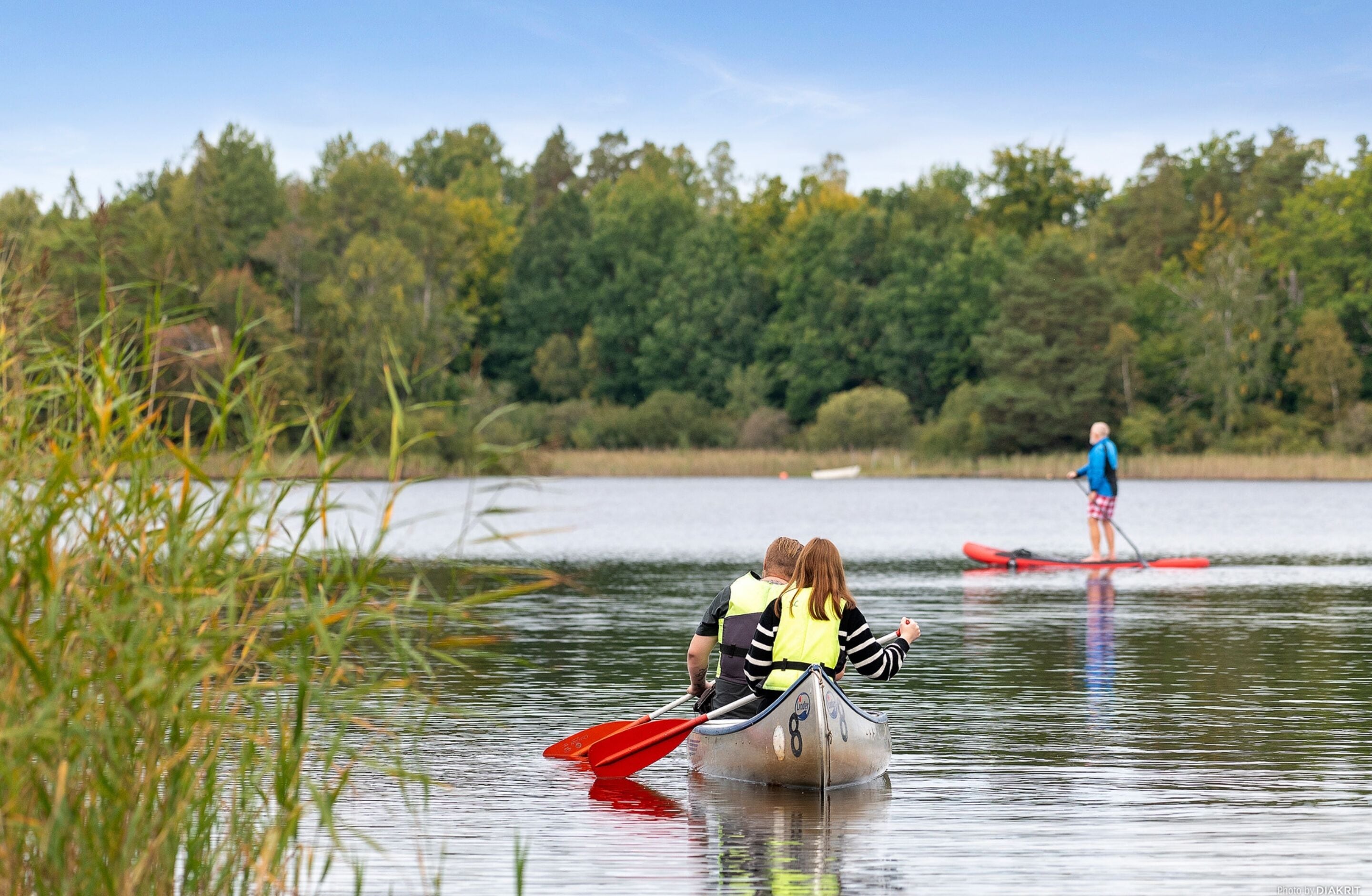 Ein ruhiger See mit zwei Kanus, eines davon mit zwei Personen und das andere mit einer Person.