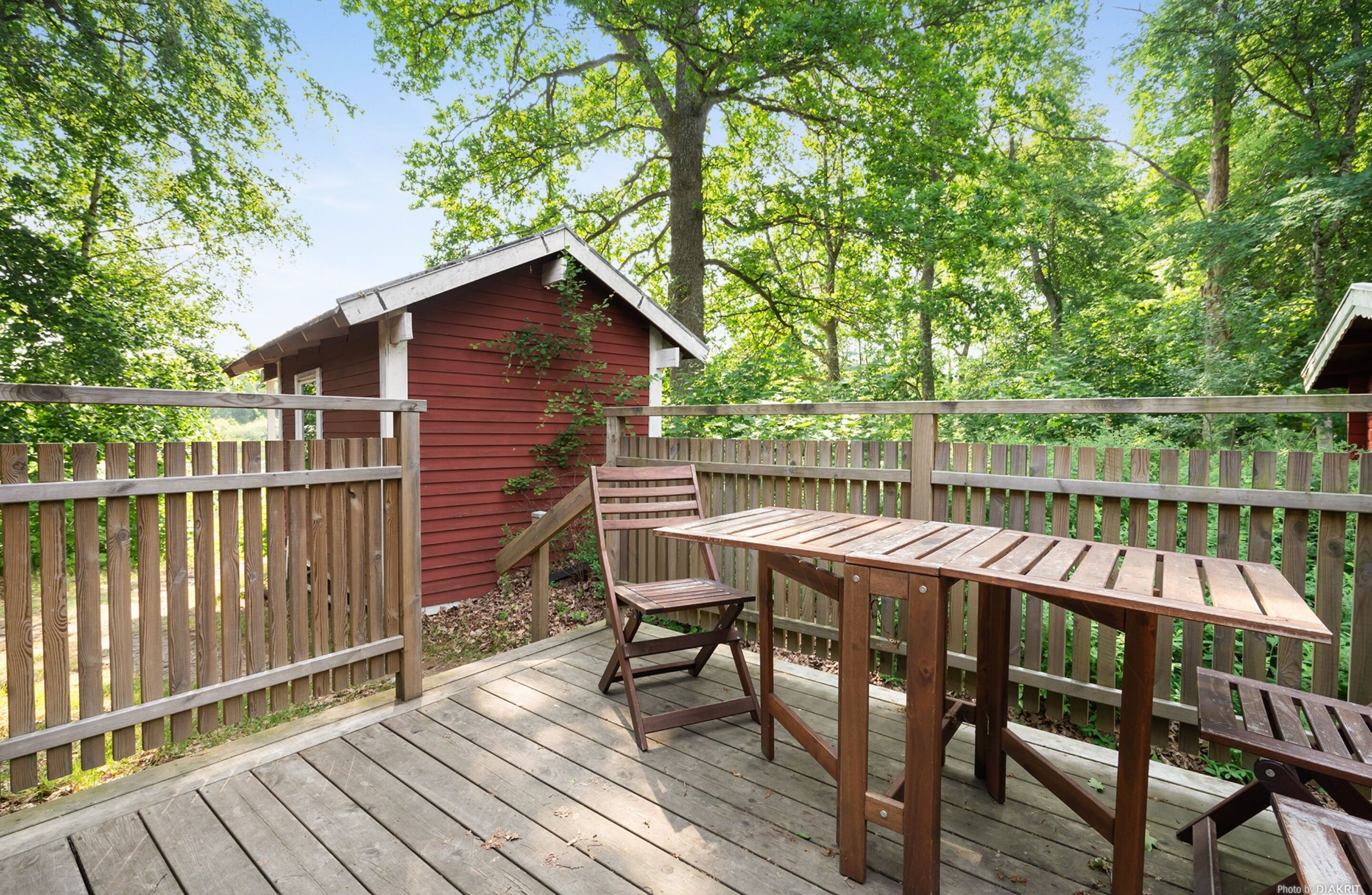 A wooden deck with a table and chairs, surrounded by a wooden fence and trees.