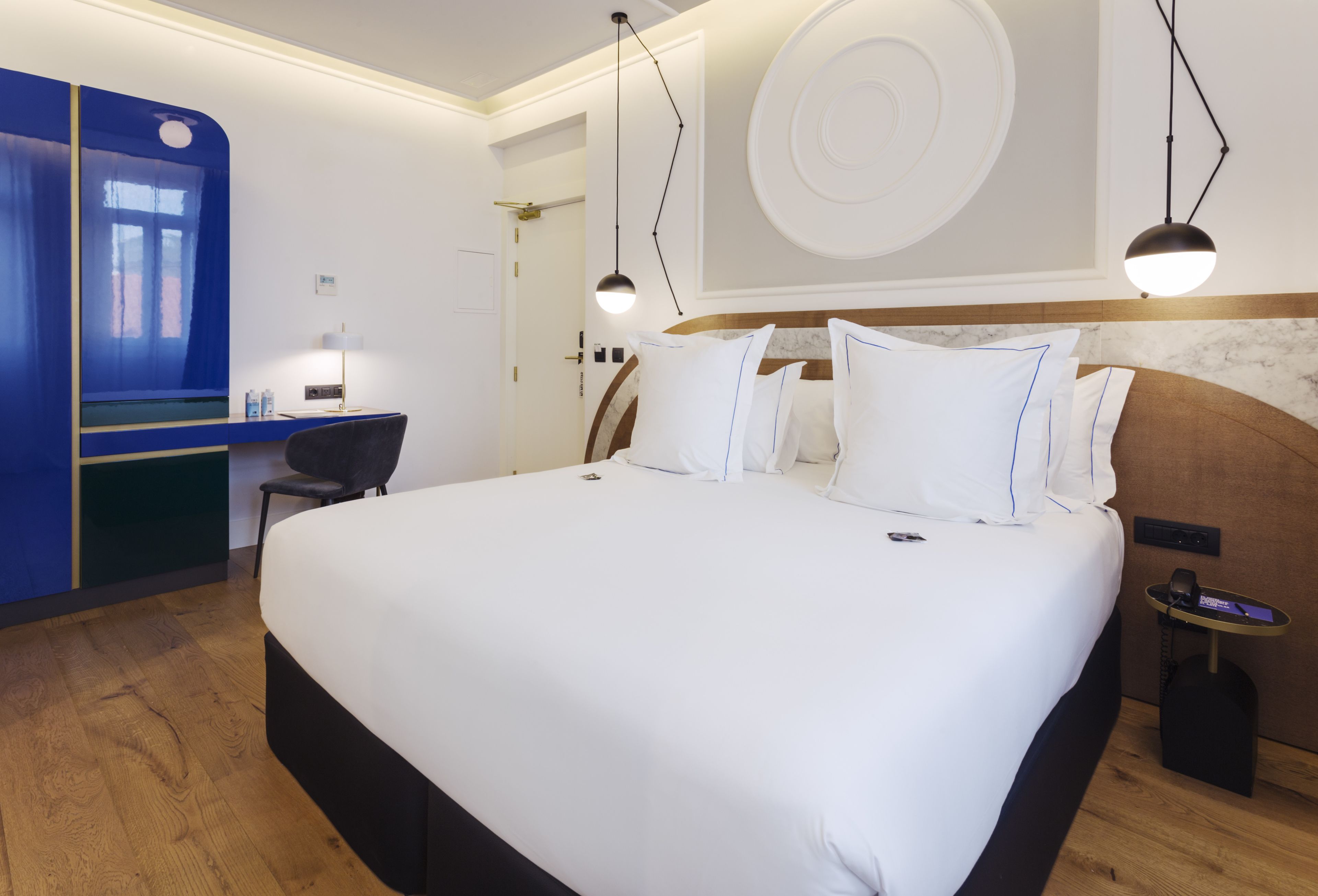 Een hotelkamer met een groot bed, nachtkastjes, een bureau en een blauwe accentmuur.