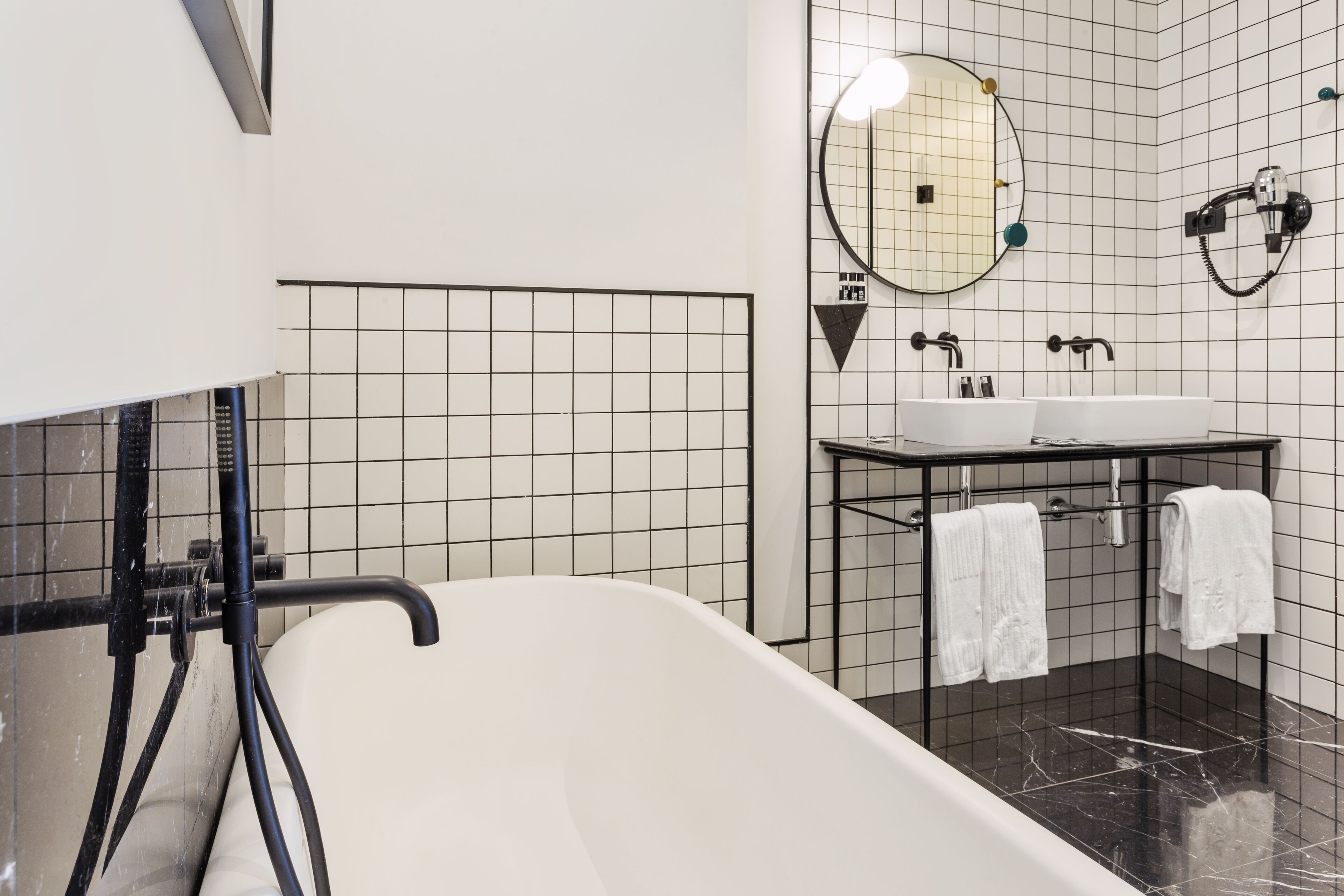 Ein modernes Badezimmer mit freistehender Badewanne, einem Waschtisch mit Spiegel und zwei Handtüchern an Haken.