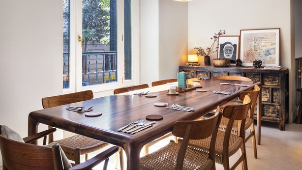 Un coin repas avec une longue table en bois, dressée pour six personnes, entourée de chaises en osier.