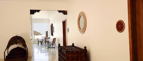 A hallway with a wooden bench, a wicker chair, and a dining area with chairs and a table.