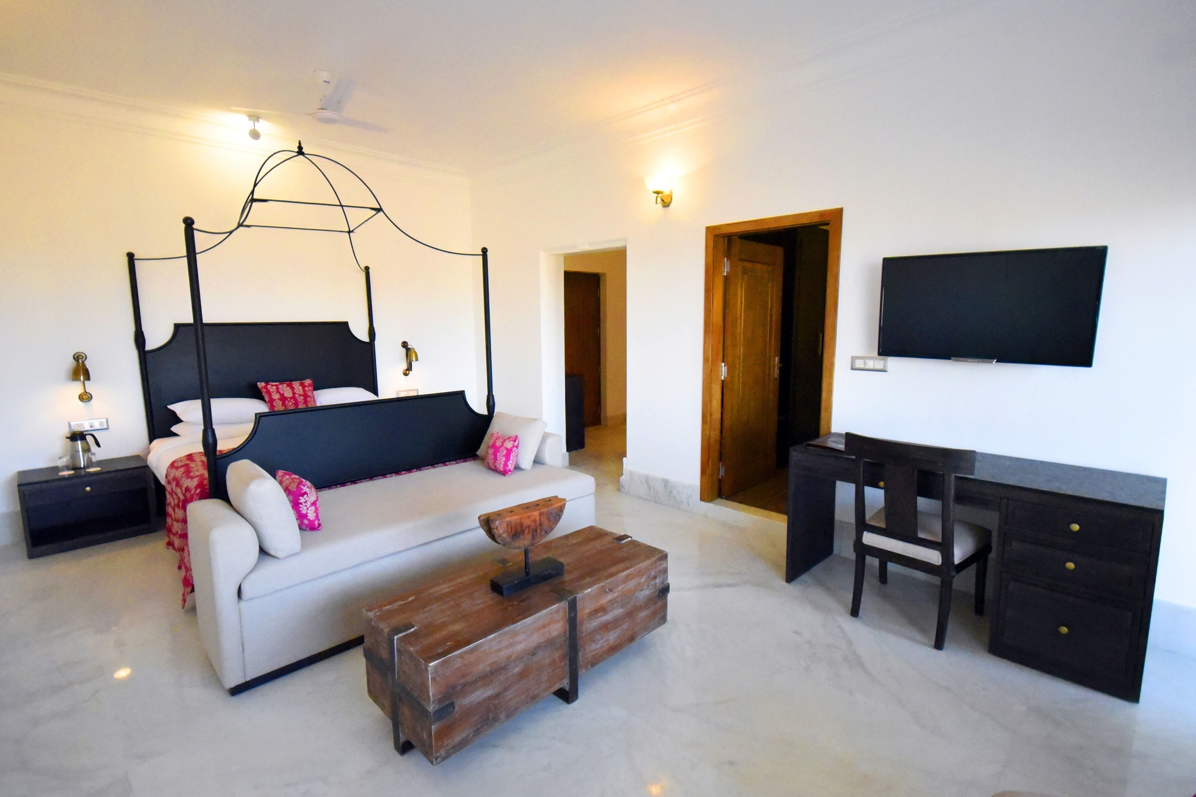 Een slaapkamer met een hemelbed, een bureau, een stoel en een televisie aan de muur.