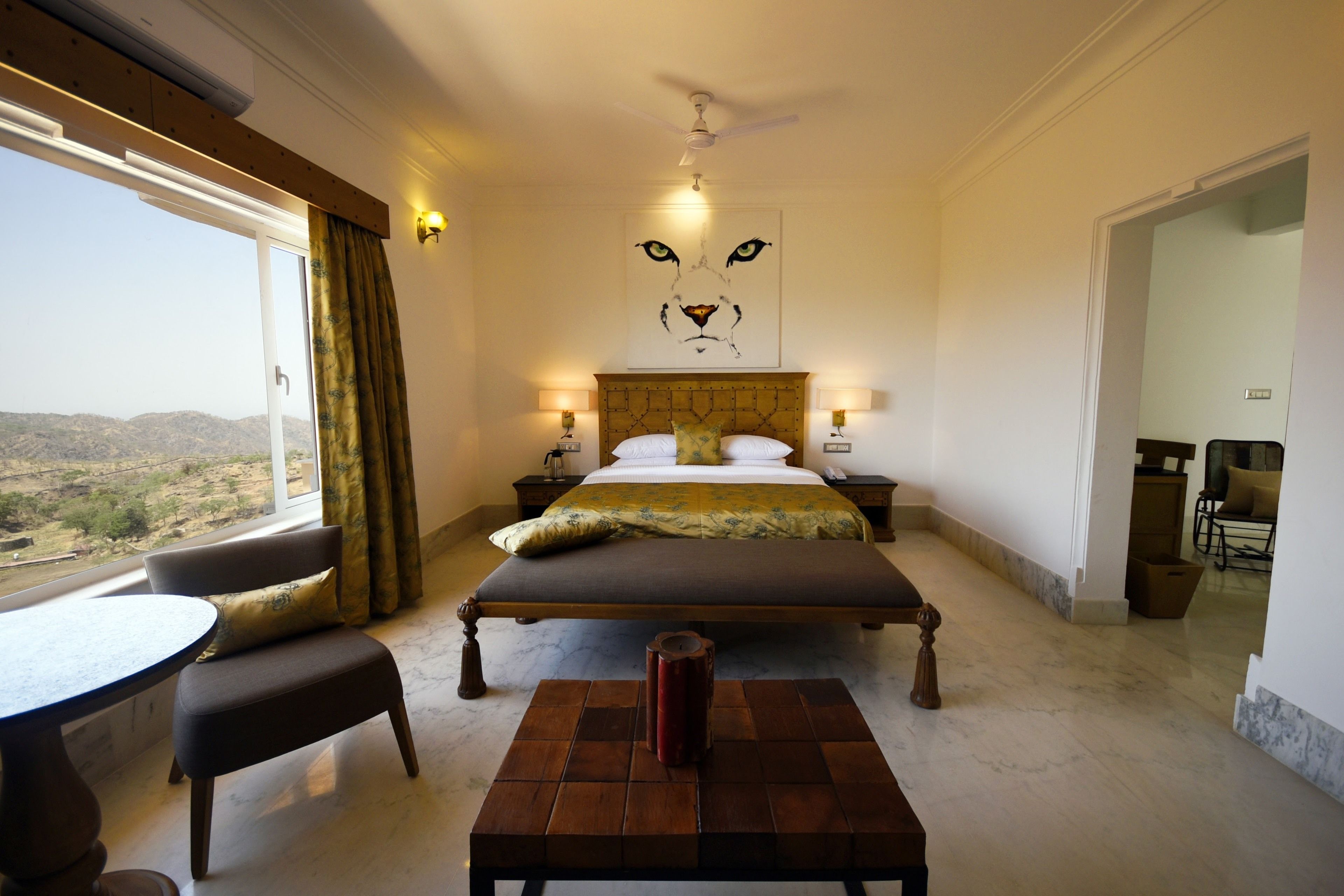 A bedroom with a large bed, a small table, a chair, and a view of the outdoors.