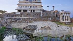 Un edificio histórico con fachada de piedra, un balcón grande y una pared de piedra circundante con columnas.