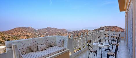 Ein Balkon mit einer Couch und Tischen, der einen Blick auf eine gebirgige Landschaft bietet.