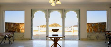 A spacious room with a large table and chairs, a chandelier, and large windows with stone walls.