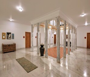 Un vestíbulo amplio con suelos de mármol, una columna decorativa central y un banco de madera.
