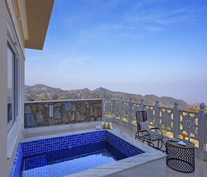 Un balcón con pared de piedra, tinaco caliente con azulejos azules y vistas a montañas.