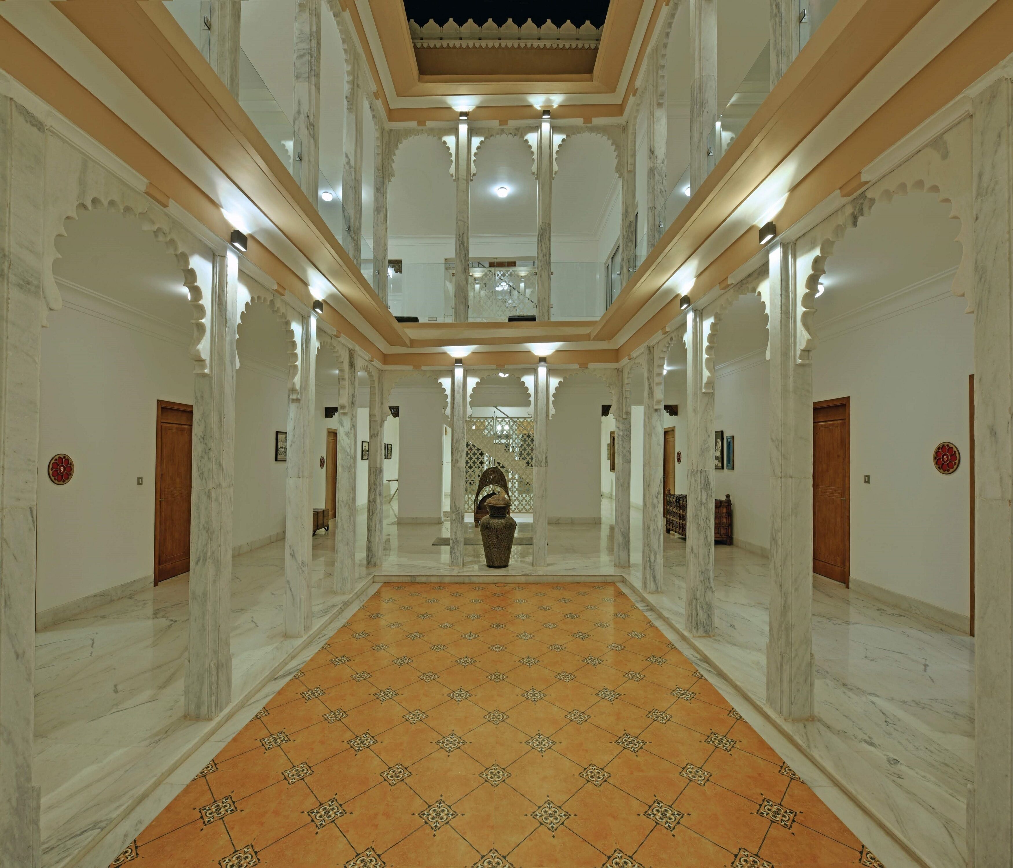 A grand hallway with marble columns, a patterned floor, and a central decorative vase.