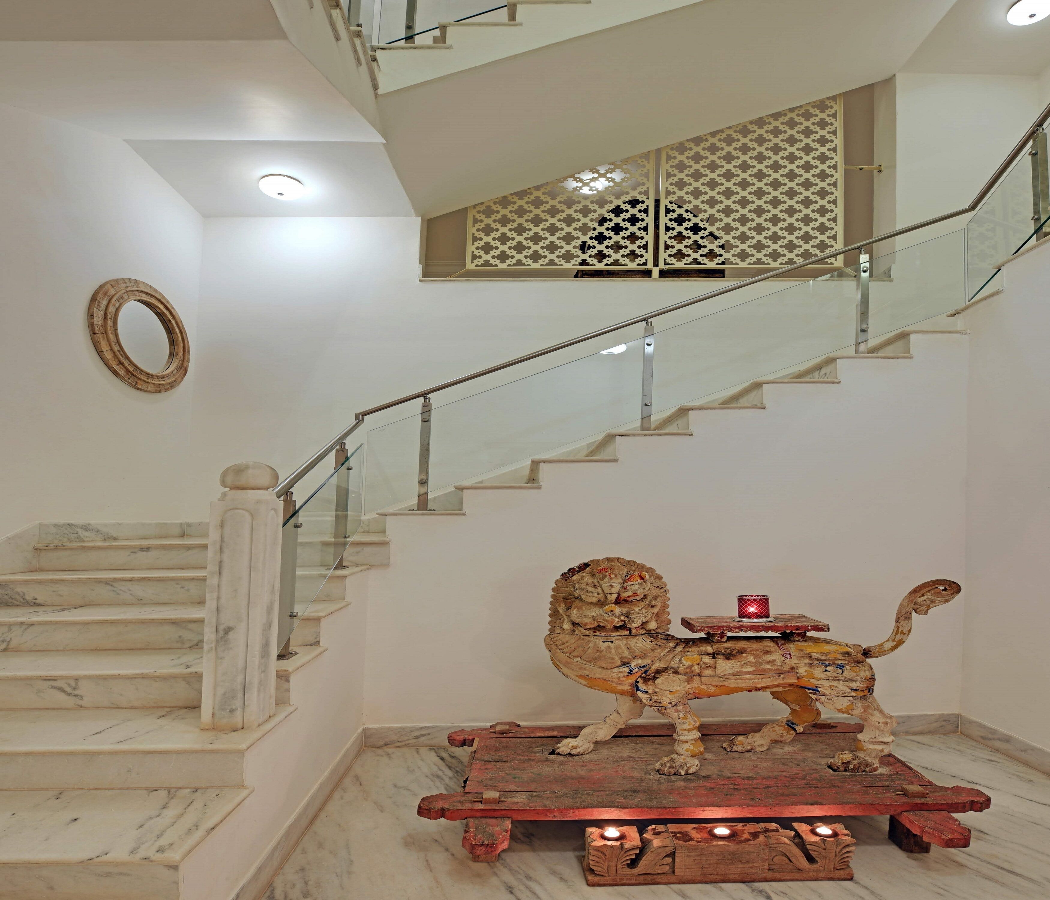 Un escalier en marbre avec des rampes en verre, une statue de lion décorative sur une plateforme en bois et un paravent orné au sommet de l’escalier.