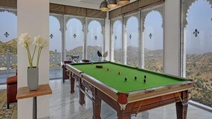 Una mesa de billar en una habitación con ventanas amplias y vistas a las colinas.