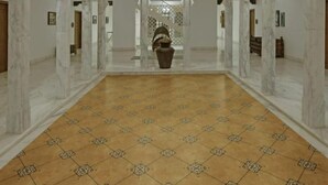 Un pasillo espacioso y ornamentado con paredes de mármol y un suelo con diseño, que conduce a una zona central con una urna decorativa.