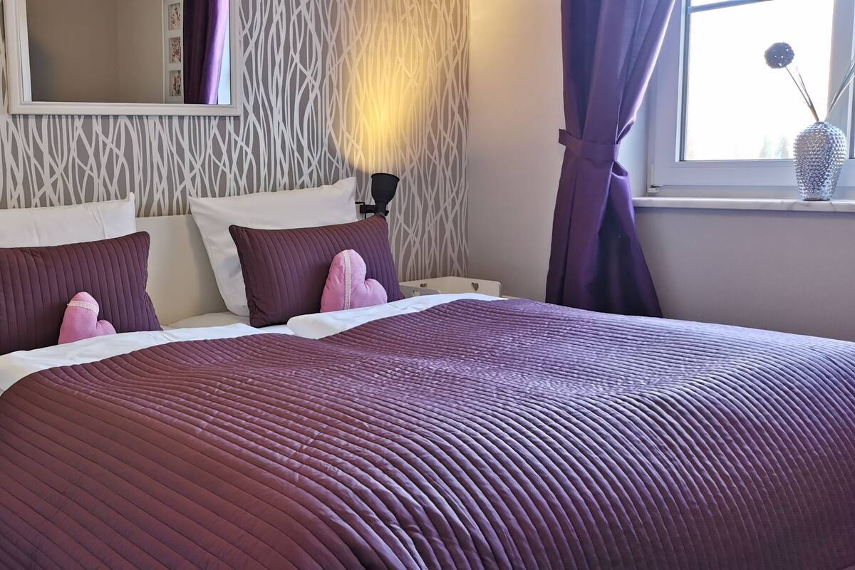 A bedroom with a bed, two bedside tables, a nightstand, a mirror, and a window with curtains.