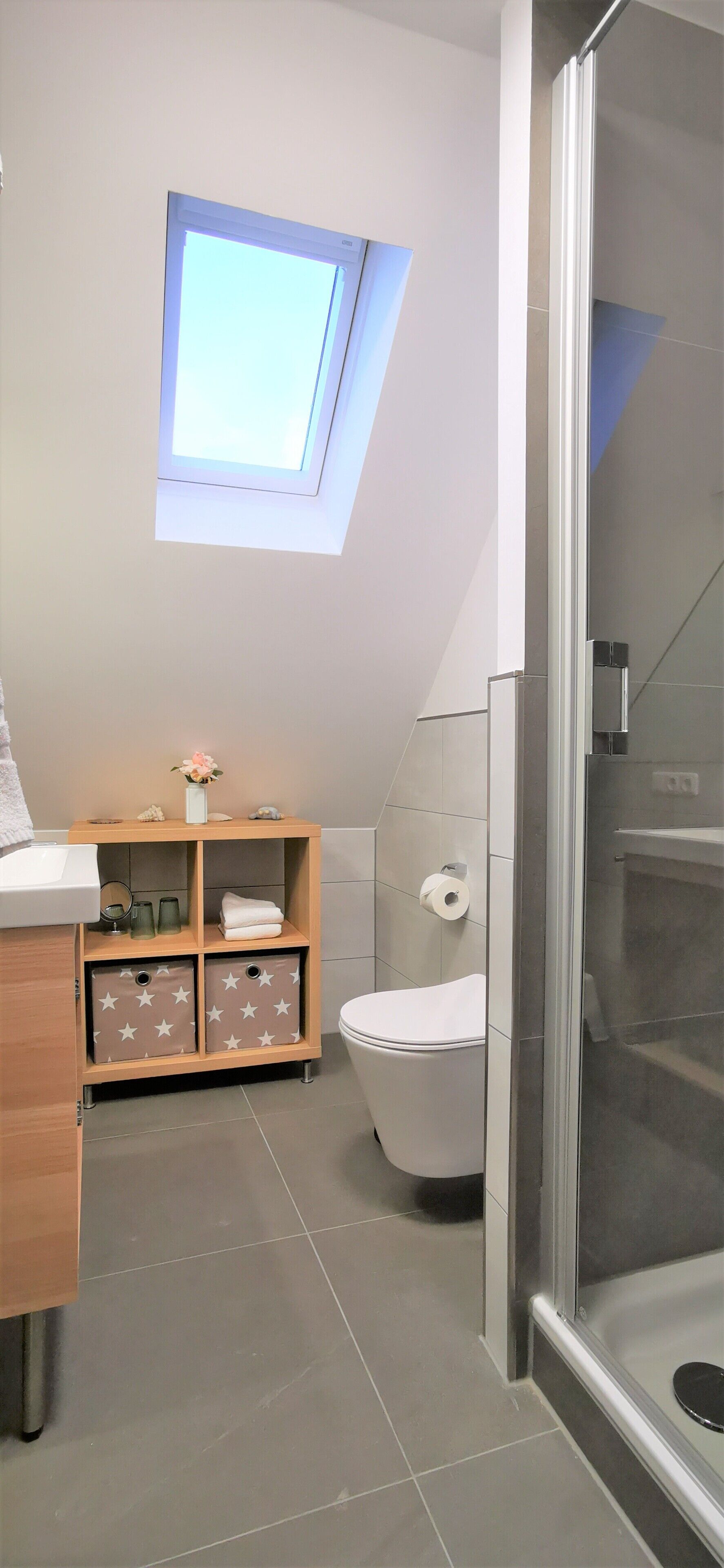 A modern bathroom with a skylight, a toilet, a shower, and a wooden storage unit with star-patterned drawers.