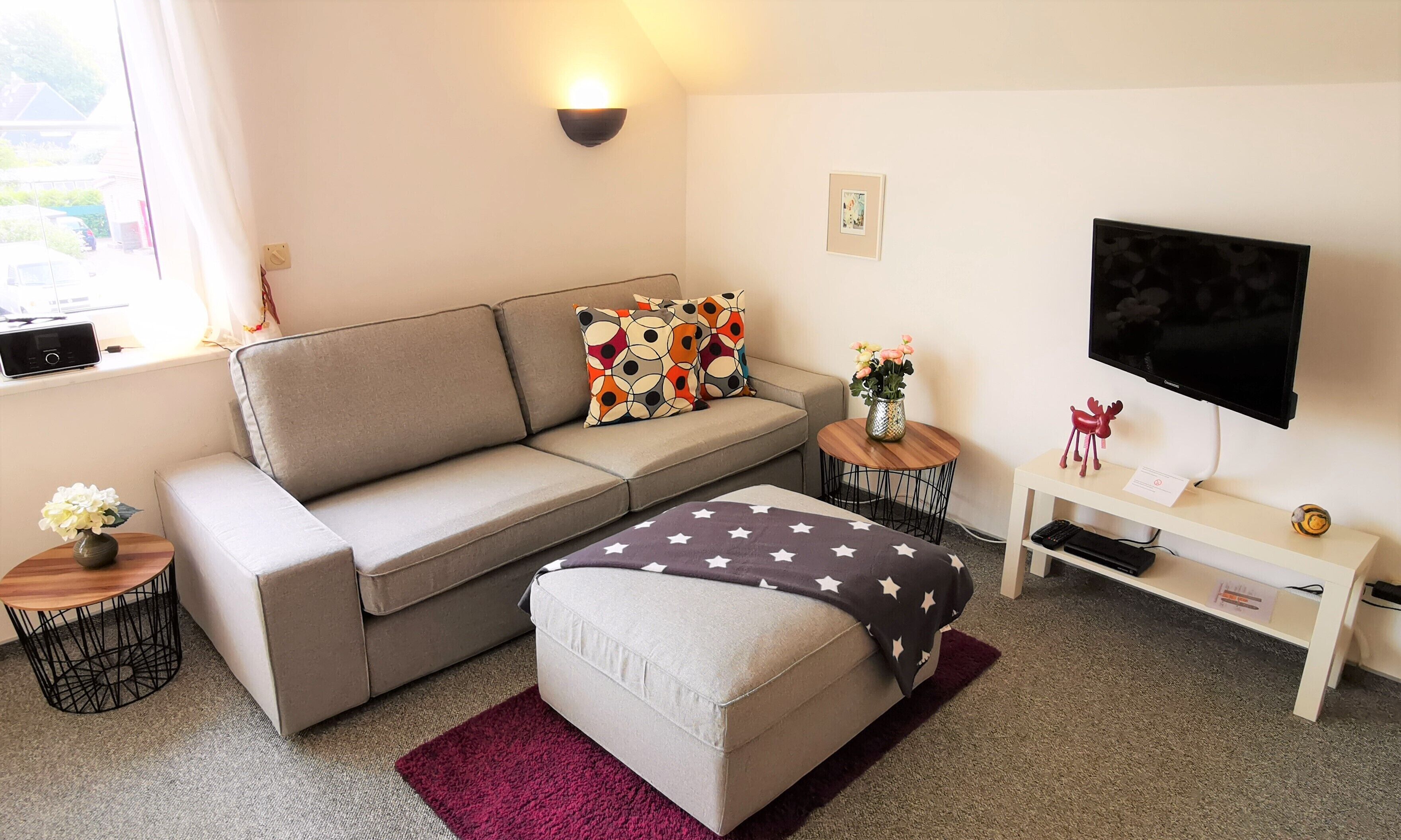 Ein modernes Wohnzimmer mit Sofa, Hocker, Couchtisch, Fernseher und Dekorationselementen.
