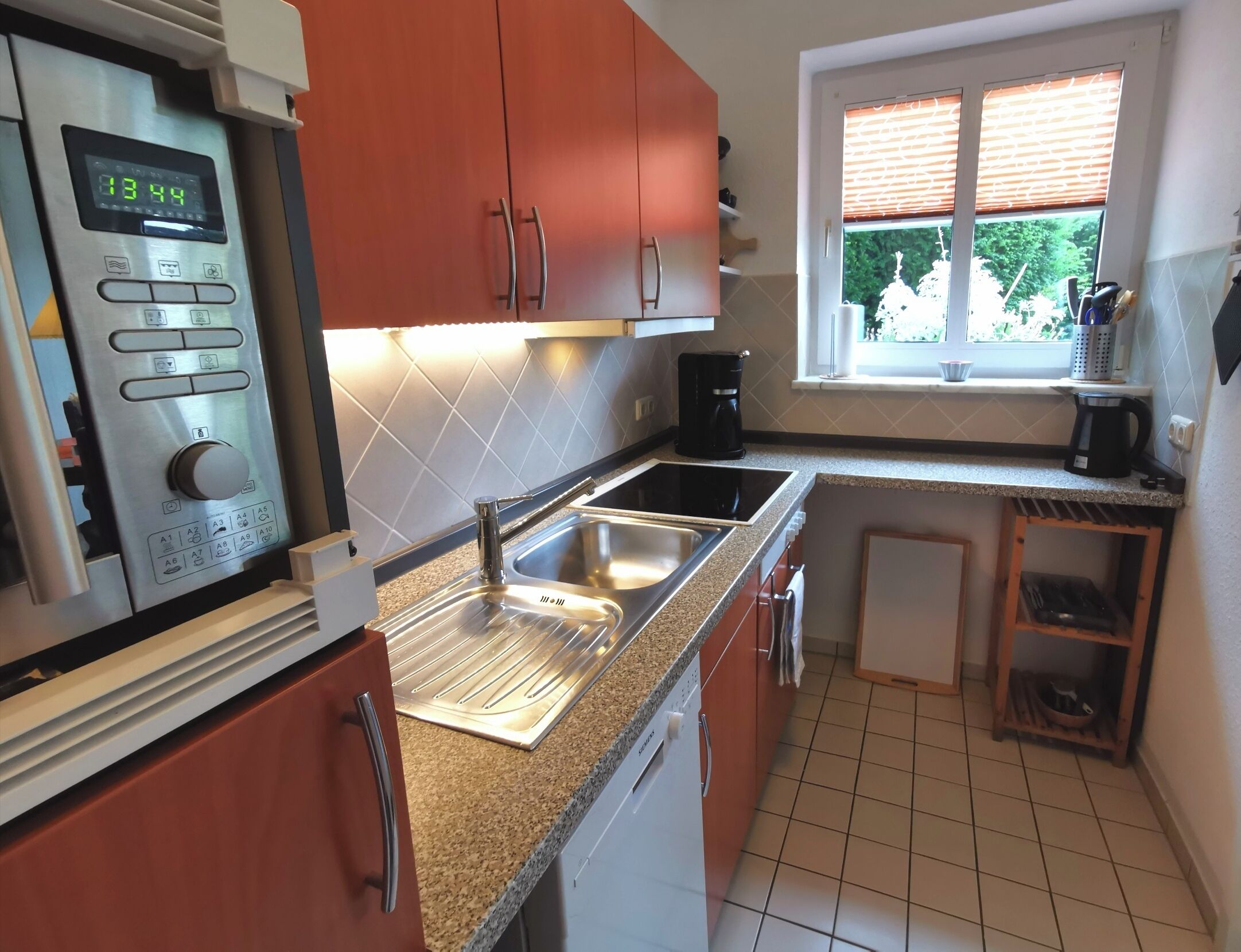 A modern kitchen with stainless steel appliances, a built-in oven, a sink, and a window with blinds.