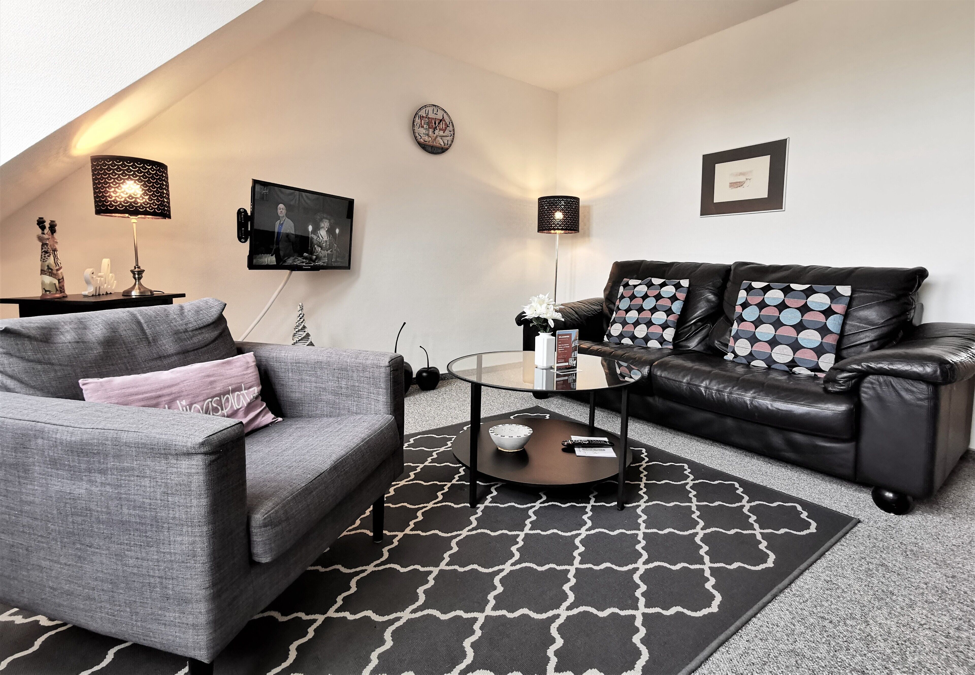 A modern living room with a grey sofa, a black leather couch, and a glass coffee table.