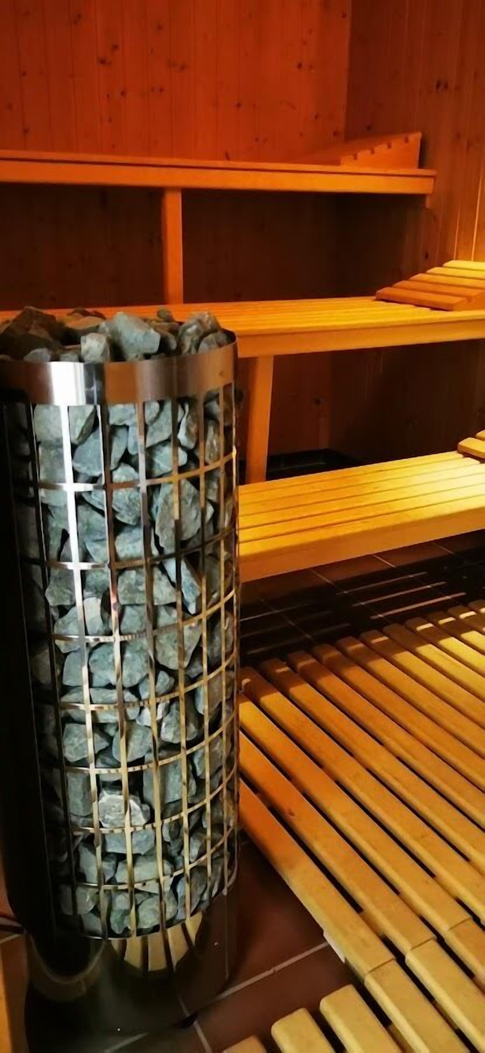Un sauna doté d’un récipient métallique rempli de pierres, de bancs en bois et d’un mur en bois.