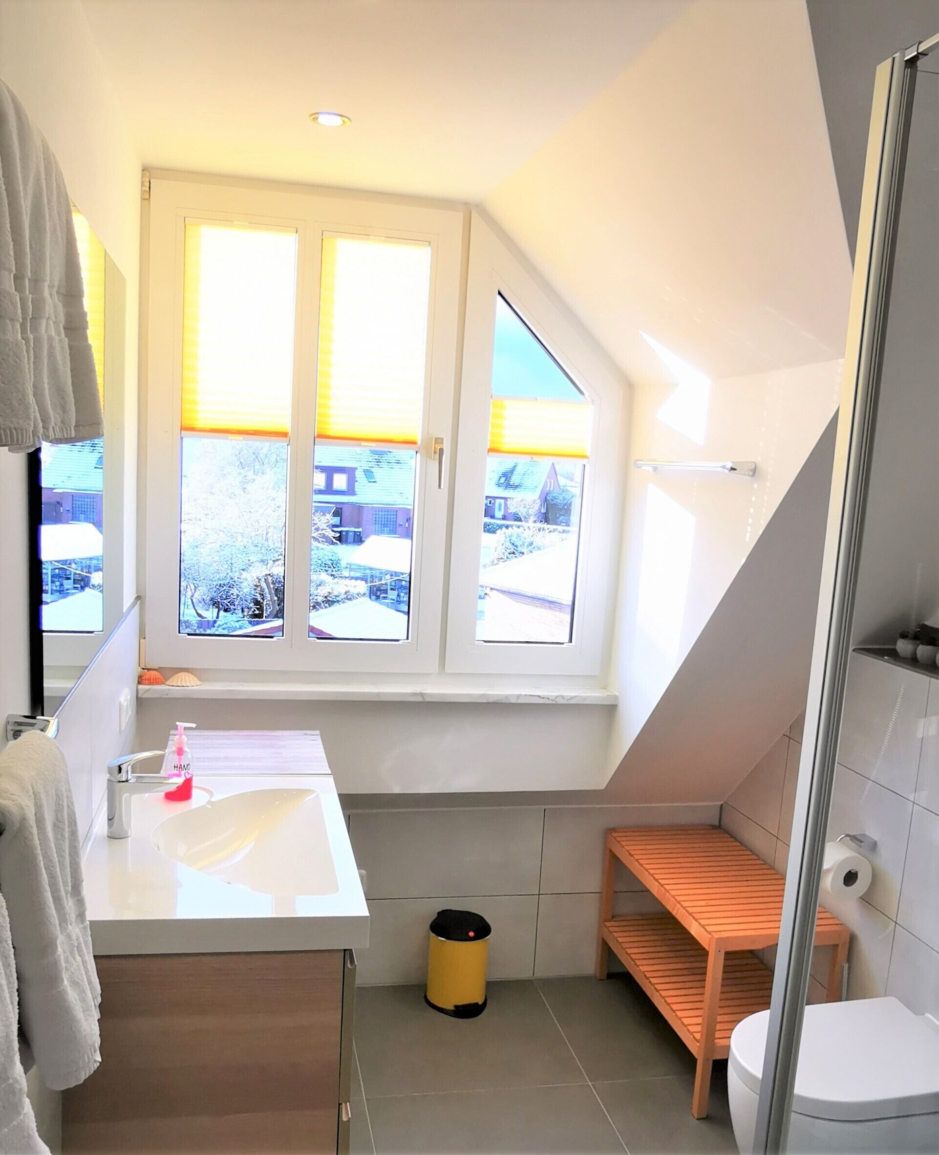 A modern bathroom with a large window, a sink, a toilet, and a shower area.