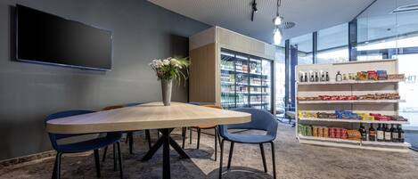 A modern meeting room with a large table, chairs, a flat-screen TV, a bookshelf, and a snack shelf.