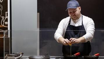 A chef in a white shirt and black apron cooking on a stove with a frying pan.