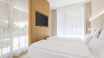 A hotel room with a large bed, a mounted TV, and large windows with sheer curtains.