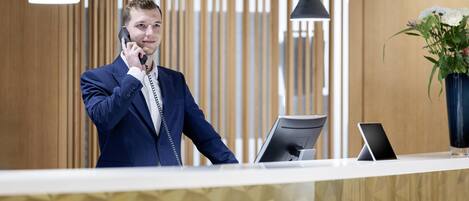 Ein moderner Hotelrezeptionstresen mit Holzvertäfelung, einer Rezeptionstheke, einem Computer und einem Telefon.