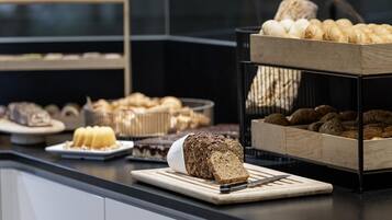 A buffet with various baked goods including bread, rolls, and pastries.