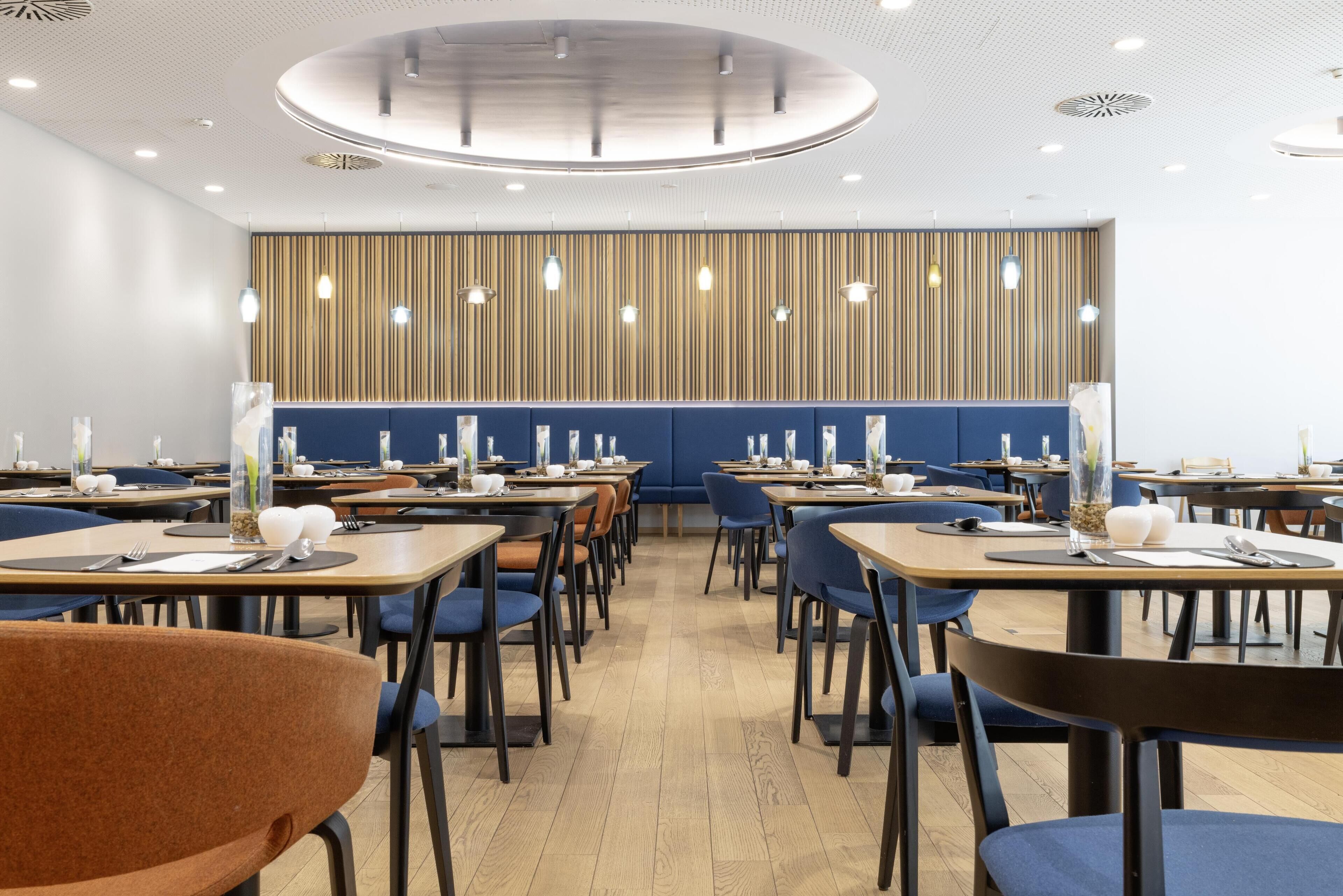 A modern dining area with wooden tables, blue chairs, and a patterned wall.