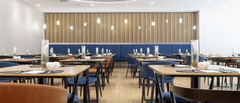 Un comedor moderno con mesas de madera, sillas azules y un papel tapiz estampado.