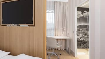 Habitación de hotel con cama, escritorio con silla, televisor y vista a un paisaje urbano a través de la ventana.