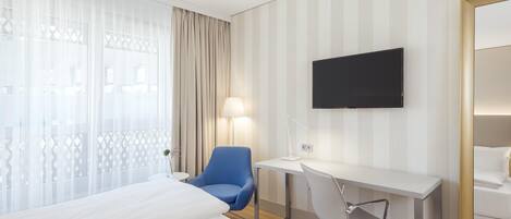 Habitación de hotel con dos camas, un escritorio, una silla, un televisor y una ventana con cortinas.