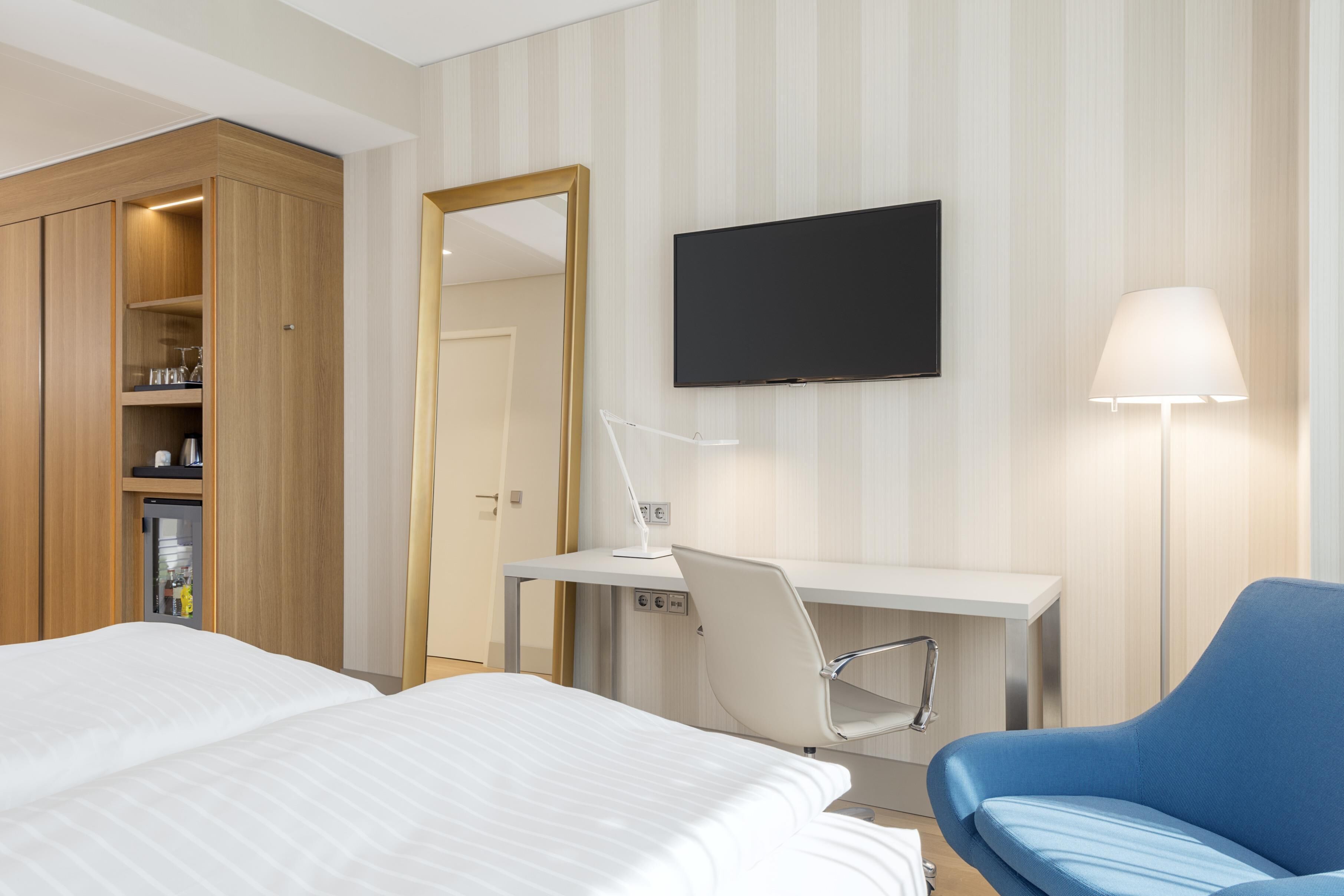 Ett hotellrum med en säng, ett skrivbord med en stol, en tv och en garderob.