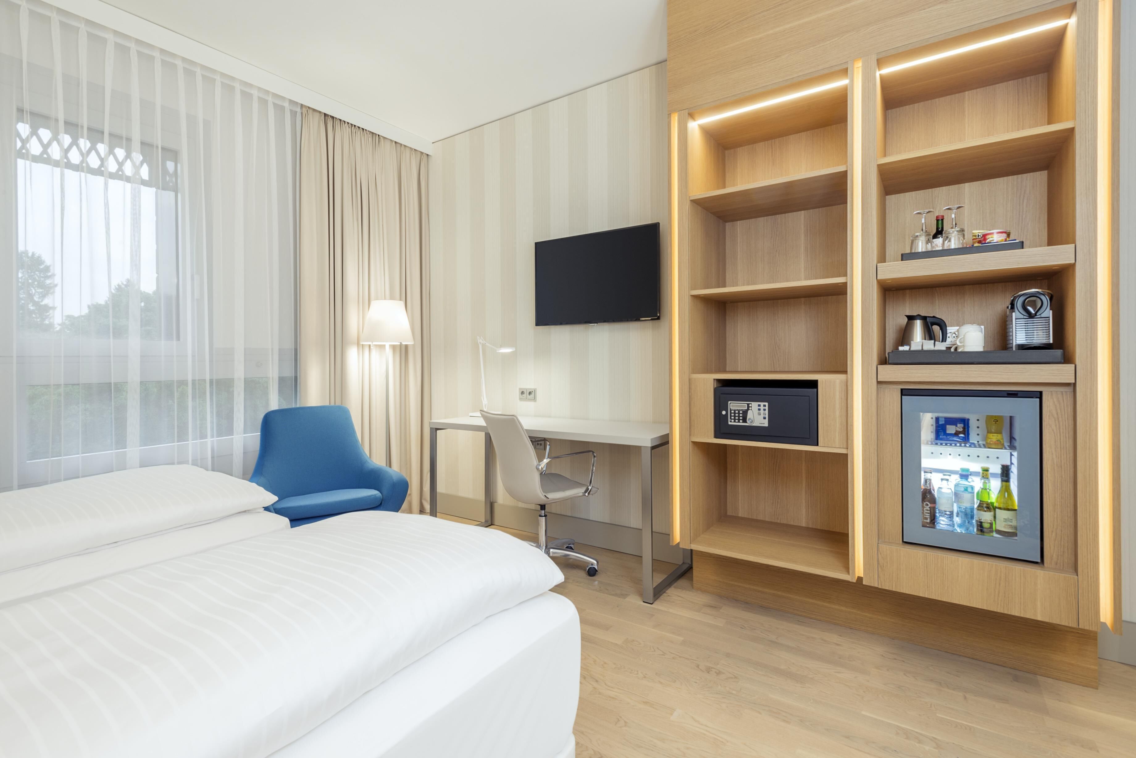 Camera d'albergo con un letto, una scrivania, una sedia, una televisione e un minibar.