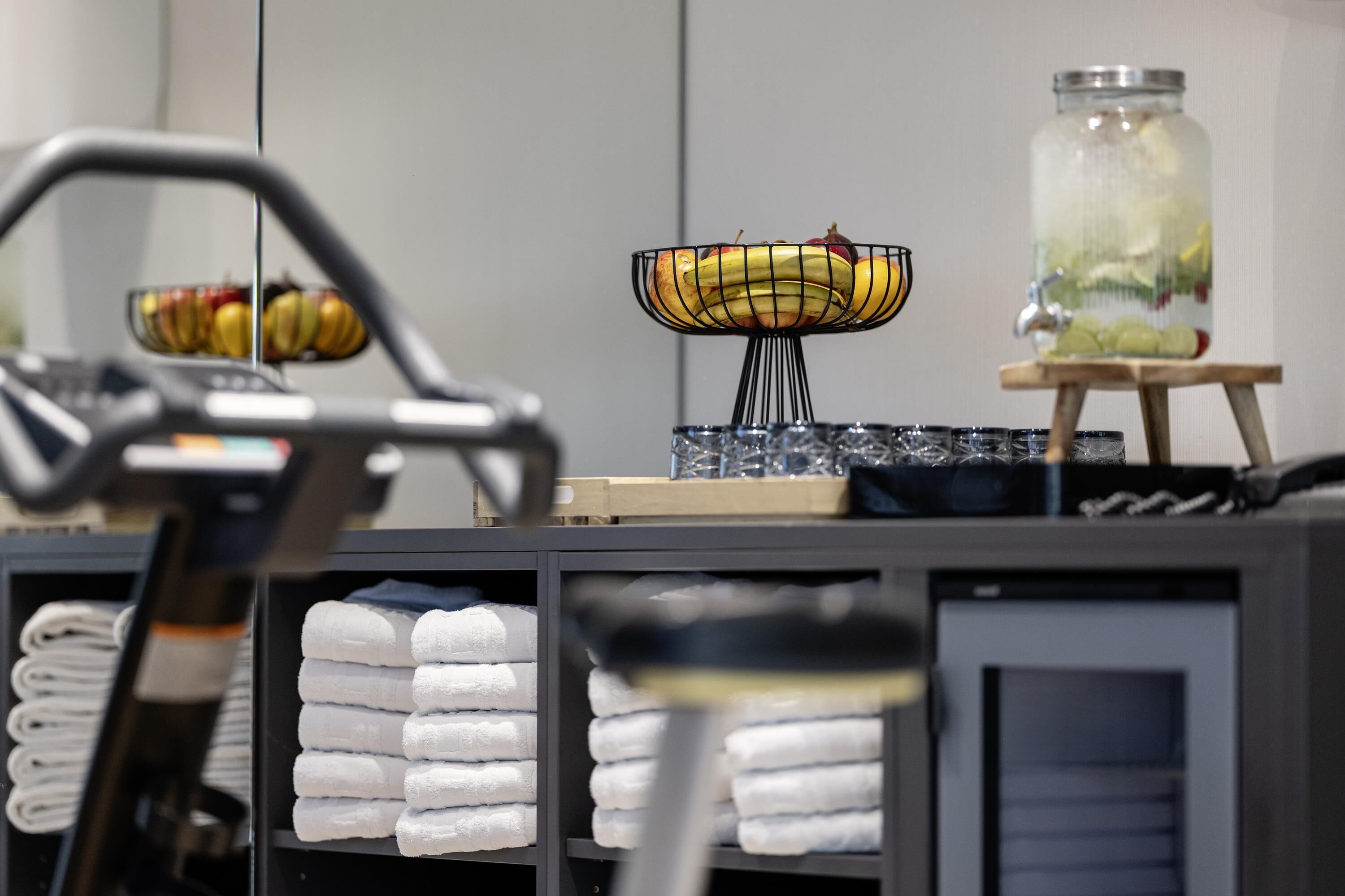 A hotel reception area with a treadmill, a fruit bowl, and neatly stacked towels.