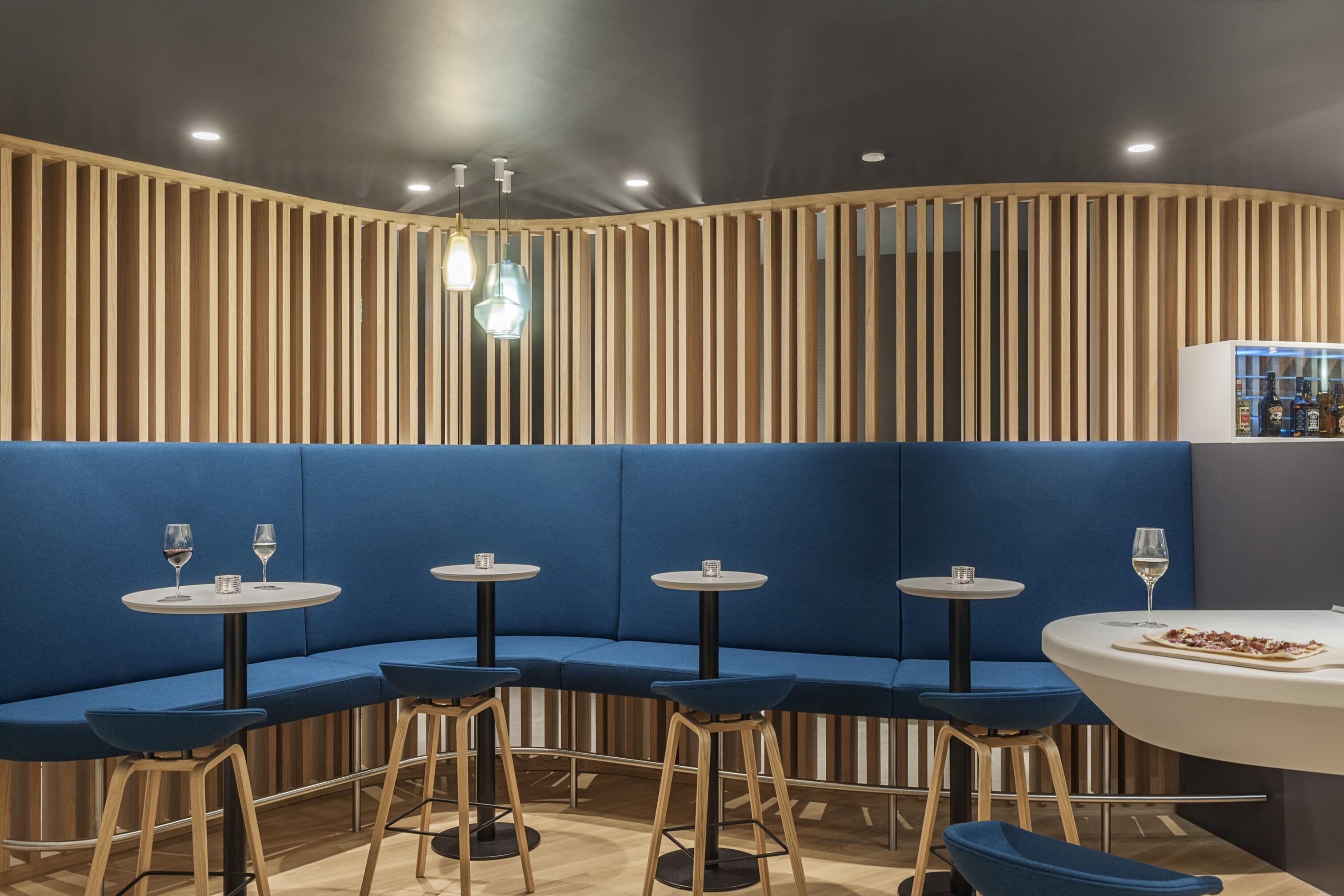 A modern restaurant with blue cushioned seating, round tables, and wooden slats on the wall.
