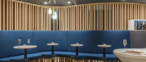 A modern restaurant with blue cushioned seating, round tables, and wooden slats on the wall.