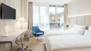 Ein Hotelzimmer mit Bett, Schreibtisch, Stuhl, Fernseher und Blick auf ein Gebäude.