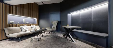 Een moderne zithoek met een bank, stoelen en een bijzettafeltje, met een houten accentwand en een donkere, beklede wand.