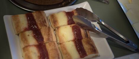 A plate of sliced cheese with tomato sauce, a knife, and a cake in the background.
