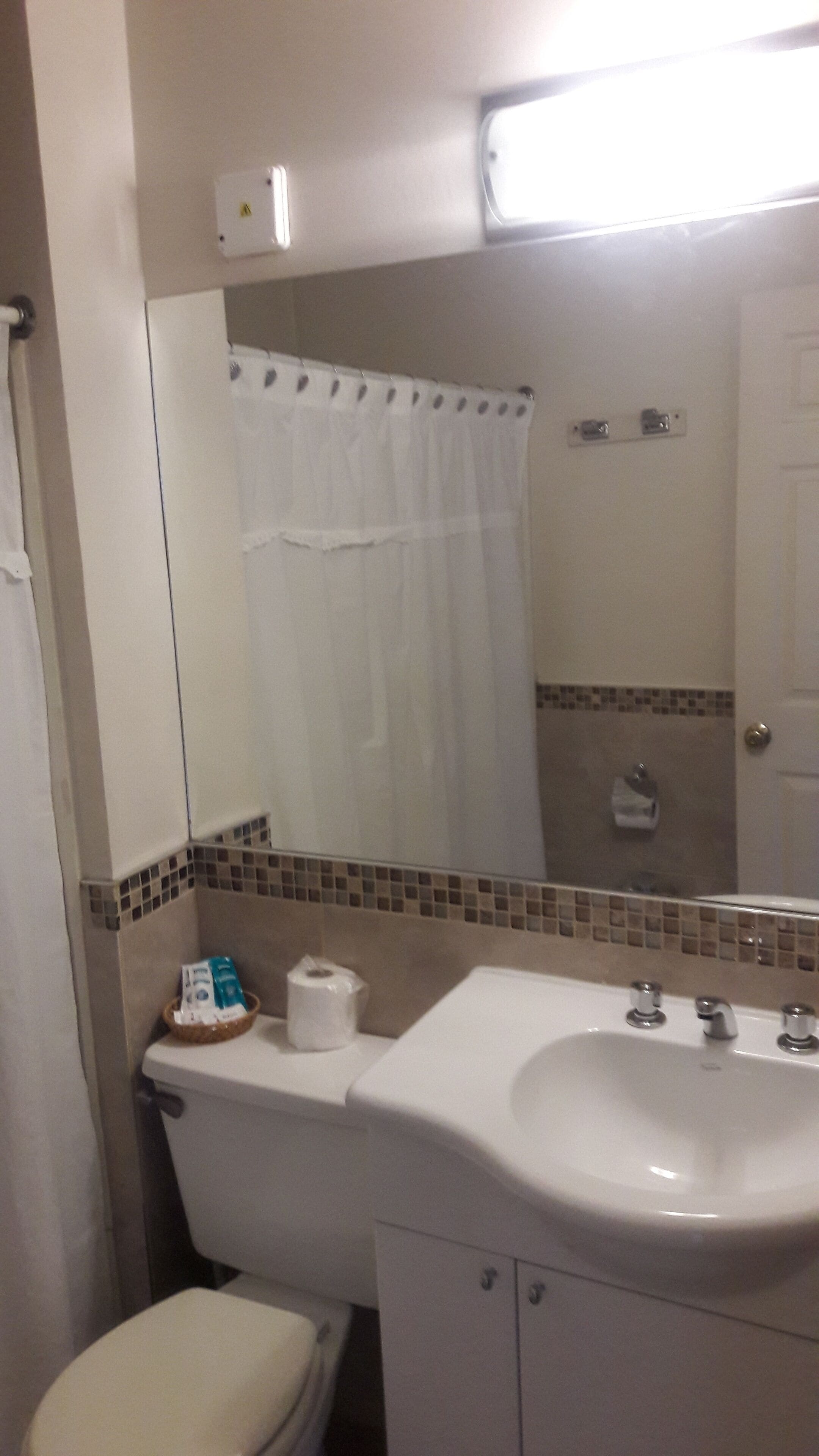 A bathroom with a toilet, sink, and mirror. There is a shower curtain, a towel, and a basket with toiletries.