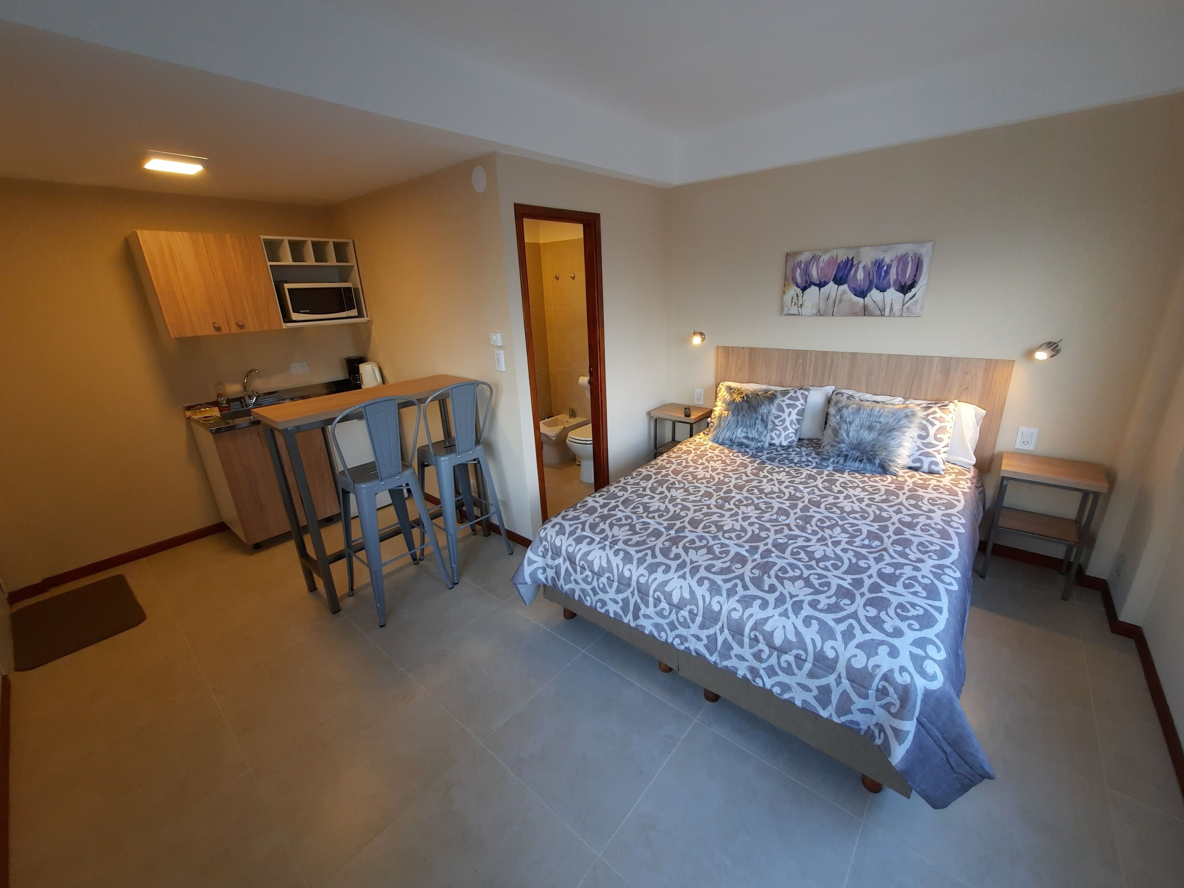 A compact hotel room with a bed, a small kitchenette, a dining area, and a bathroom.